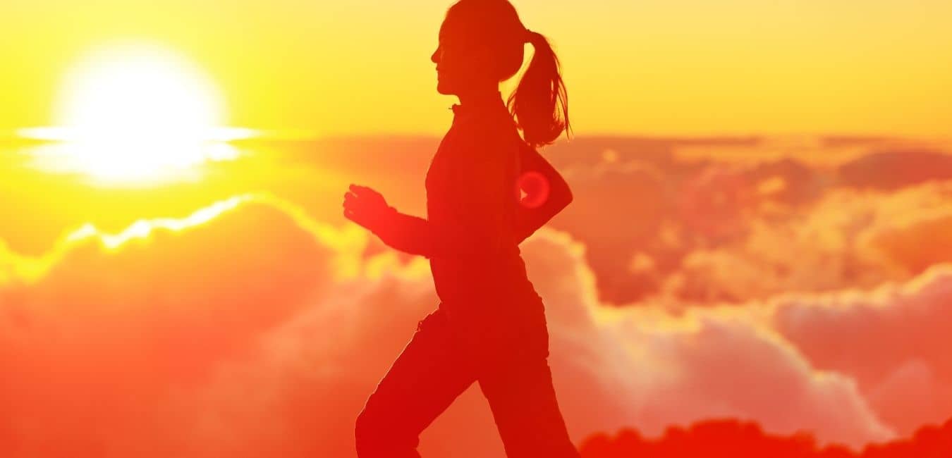 Hand weight exercises. Silhouette of a woman walking with sun and clouds in the background.