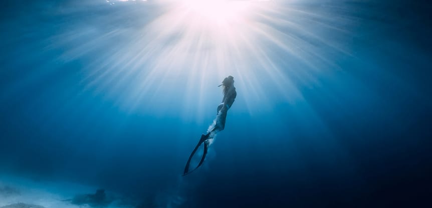 Pushing Limits Freediving: Interview with Katie Coeckelenbergh-Sawyer woman freediving in blue water swimming towards surface, sun overhead