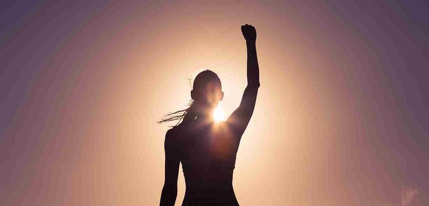 Finding Your Fitness Confidence Interview with Fit is Freedom Alumni Jennifer. Silhouette of a woman with right arm raised standing in front of the sun.