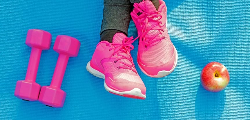 How to Get Fit: The Right Questions for the Best Workout. Woman wearing hot pink gym shoes next to hot pink hand weights and an apple on a blue exercise mat.