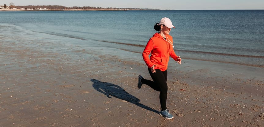 The Number 1 Question You Should be Asking Yourself Daily for Your Health and Fitness. Woman in orange hoodie jogging on beach.