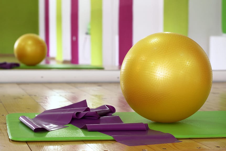 Indoor home workout equipment. Resistance band and exercise ball on green yoga mat in an exercise studio.