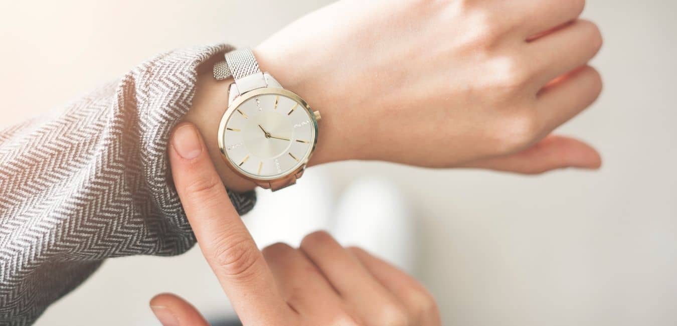 Finding time to exercise. Woman pulling up sleeve of her gray sweater to check the time on her wrist watch.