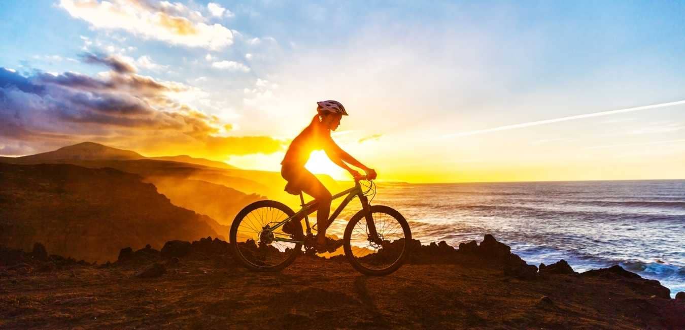A Completely NEW Way to Train for Your Fitness. Woman on mountain bike in front of setting sun.